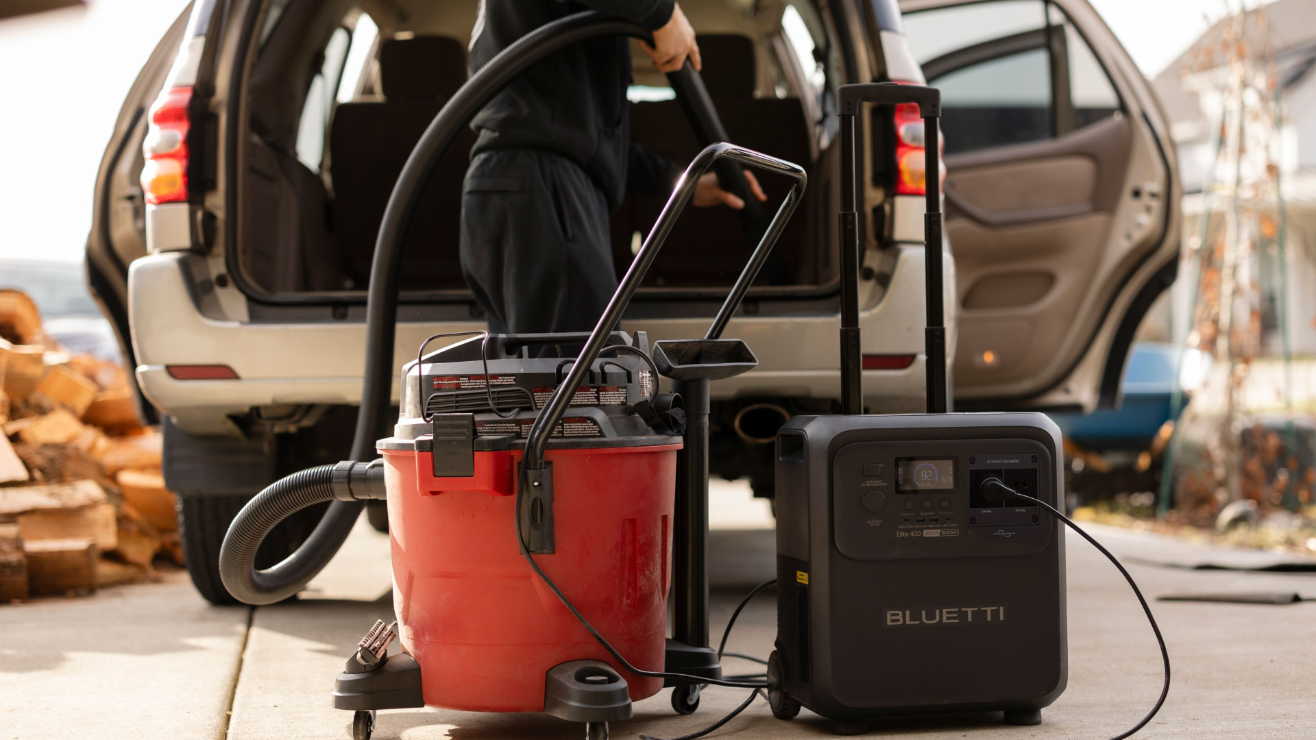 Man vacuuming the rear boot area of a car, with vacuum cleaner in forrground and plugged into a portable power station.