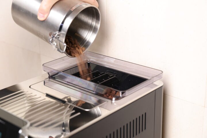 Dumping coffee beans into hopper at top of De'Longhi PrimaDonna