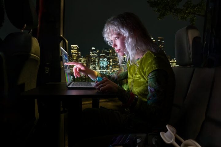 Person touching the screen of a MacBook Pro at night with city lights in the background