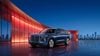Blue HongQi E-HS9 electric SUV parked beside a modern building with a city skyline at dusk